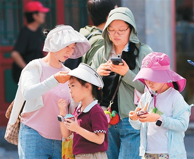 近日，在北京前門大街，游客通過戴帽子、穿防曬服抵擋烈日。   新華社記者 鞠煥宗攝