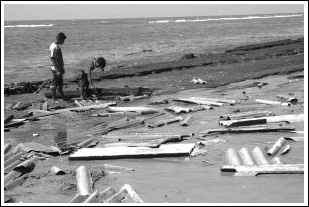 2004年12月26日，在斯里蘭卡首都科倫坡，兩位當地居民途經被沖到海邊的屋頂碎片。（圖片來源：新華社記者陳占杰攝）