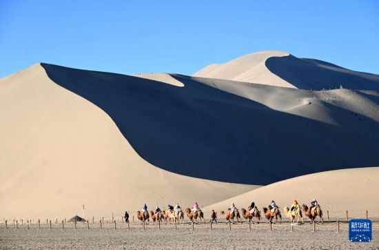 5月10日，游客乘騎駱駝在甘肅省敦煌市鳴沙山月牙泉景區游覽。新華社發（張曉亮 攝）